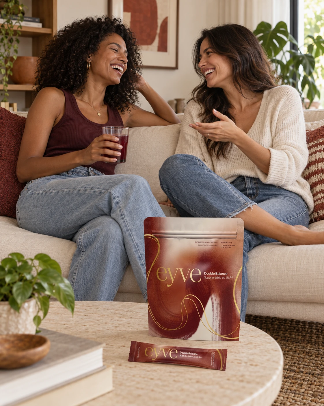 Duas mulheres conversando no sofá, uma delas com um copo da bebida EYVE, com o pouch EYVE na mesa